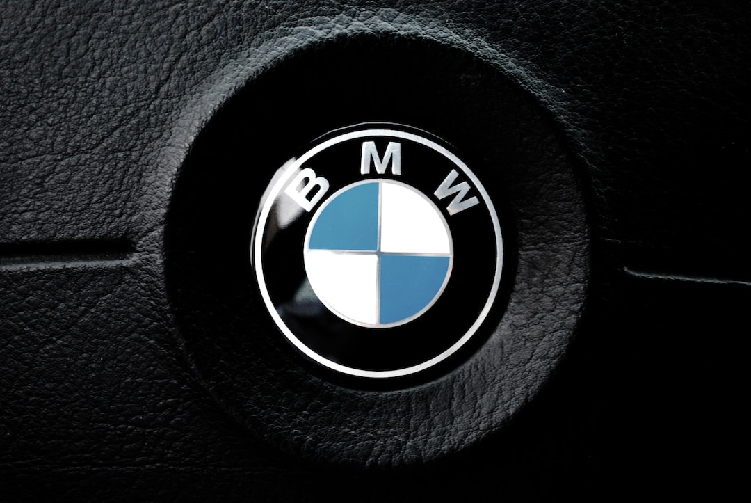 תקריב של לוגו BMW על הגה עור שחור של רכב, מרשים כמו לוח מחוונים פרימיום של WordPress Hosting. הסמל כולל עיגול המחולק לרבעים כחולים ולבנים עם האותיות BMW בחלק העליון.